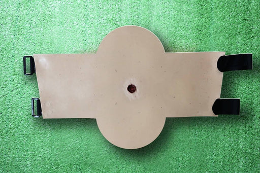 A beige, padded medical device rests on a green surface. It features two black, lateral supports and a central circular cutout.