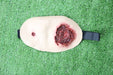 A realistic fake wound, showing simulated bleeding and puncture, rests on artificial turf.