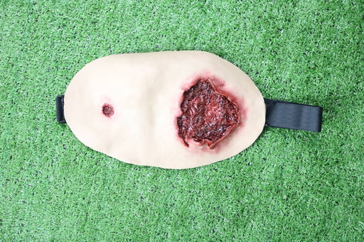 A realistic fake wound, showing simulated bleeding and puncture, rests on artificial turf.