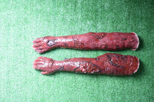 Two artificial arms, appearing burned, lie on artificial turf.