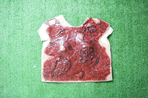 A simulated wound rests on artificial turf. The prosthetic, shaped like a torso, is colored reddish-brown to mimic injured flesh.