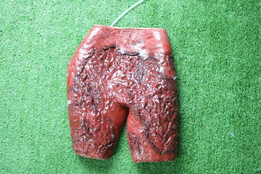 A textured, red, shorts-shaped object rests on artificial turf. A thin, light-colored tube is attached to its top.