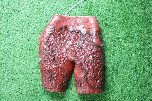 A textured, red, shorts-shaped object rests on artificial turf. A thin, light-colored tube is attached to its top.