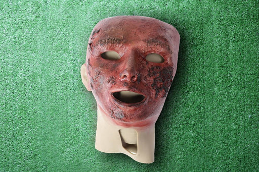 A realistic-looking mask, depicting a severely burned human face, rests against a mottled green background.