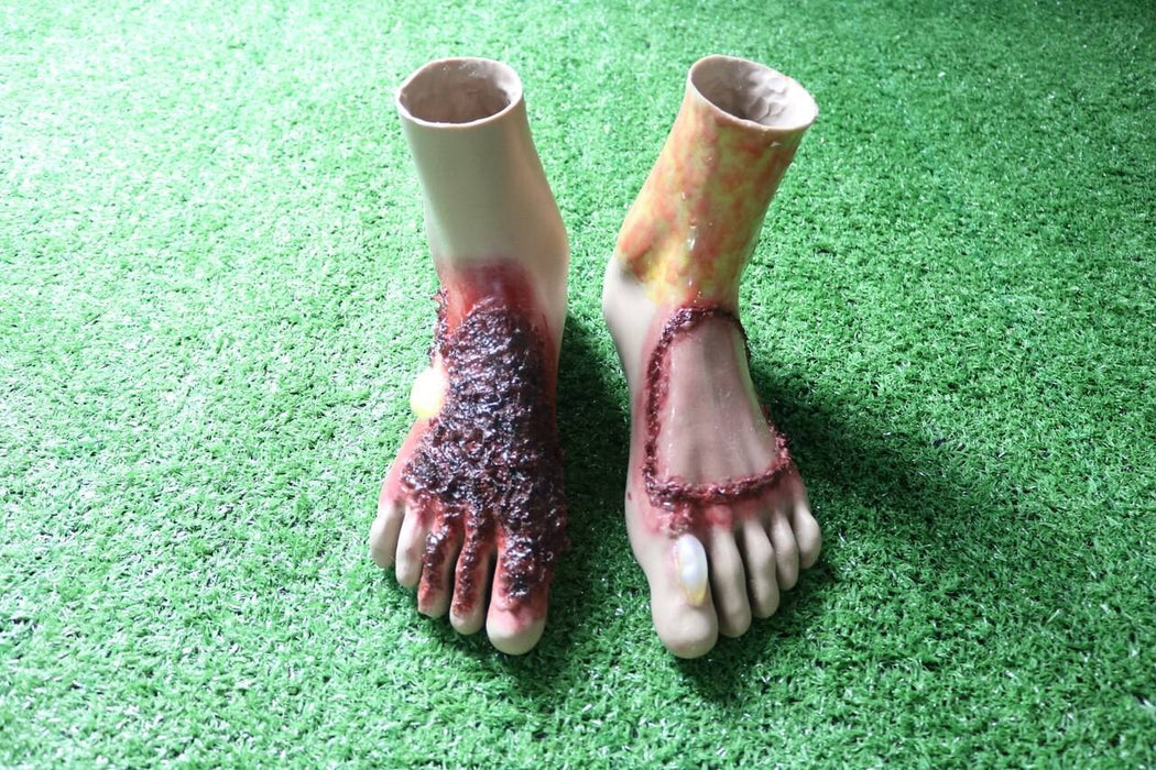 Two prosthetic feet, depicting severe burns and wounds, rest on artificial turf.