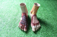 Two prosthetic feet, depicting severe burns and wounds, rest on artificial turf.