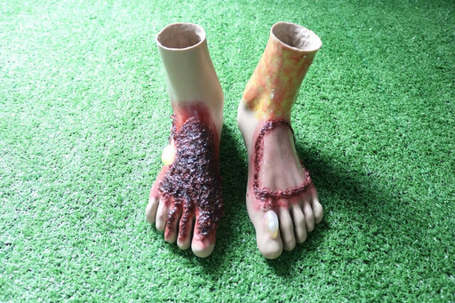 Two prosthetic feet, depicting severe burns and wounds, rest on artificial turf.