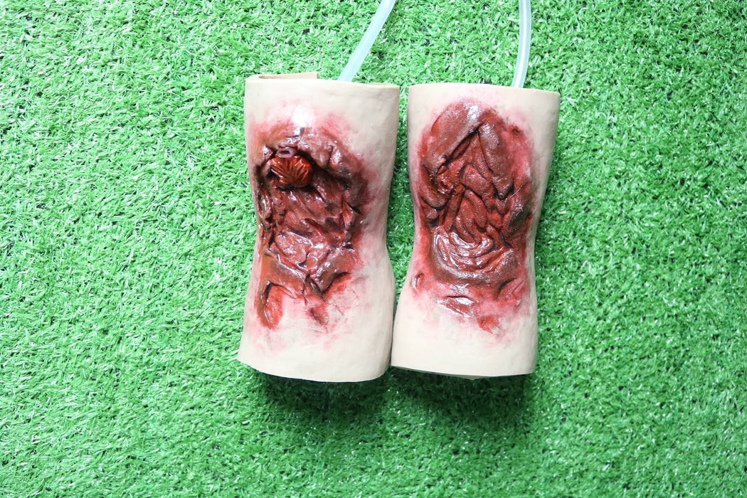 Two small, cylindrical objects, resembling realistic depictions of wounds, hang against a green, textured background.