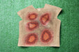 A sleeveless shirt depicting simulated wounds rests on artificial turf. The wounds are painted in shades of red and brown, suggesting injury.