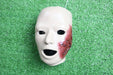 A realistic face mask, displaying a bloody injury, rests on artificial turf.