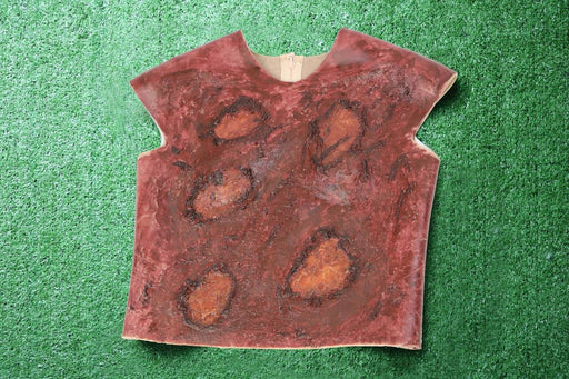 A sleeveless, maroon garment with simulated burn marks rests on artificial turf.