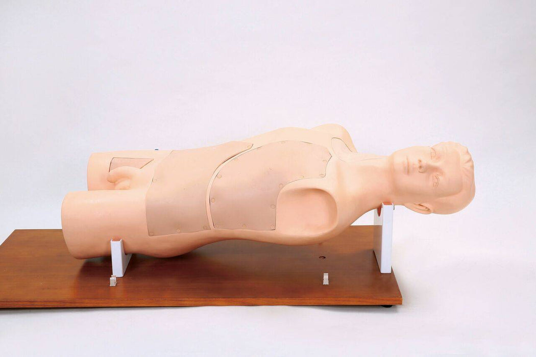 A light-skinned CPR manikin rests on a wooden surface. A white surface extends from the left side of the wood. The background is a blank, white space.