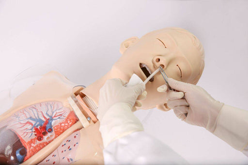 A medical dummy lies in a supine position while a gloved hand inserts a tool into its nasal passage, simulating a medical procedure, on a white table.