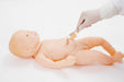 A baby mannequin lies on a white surface, while a gloved hand reaches toward its stomach with a cotton-tipped instrument, possibly cleaning the umbilical area.