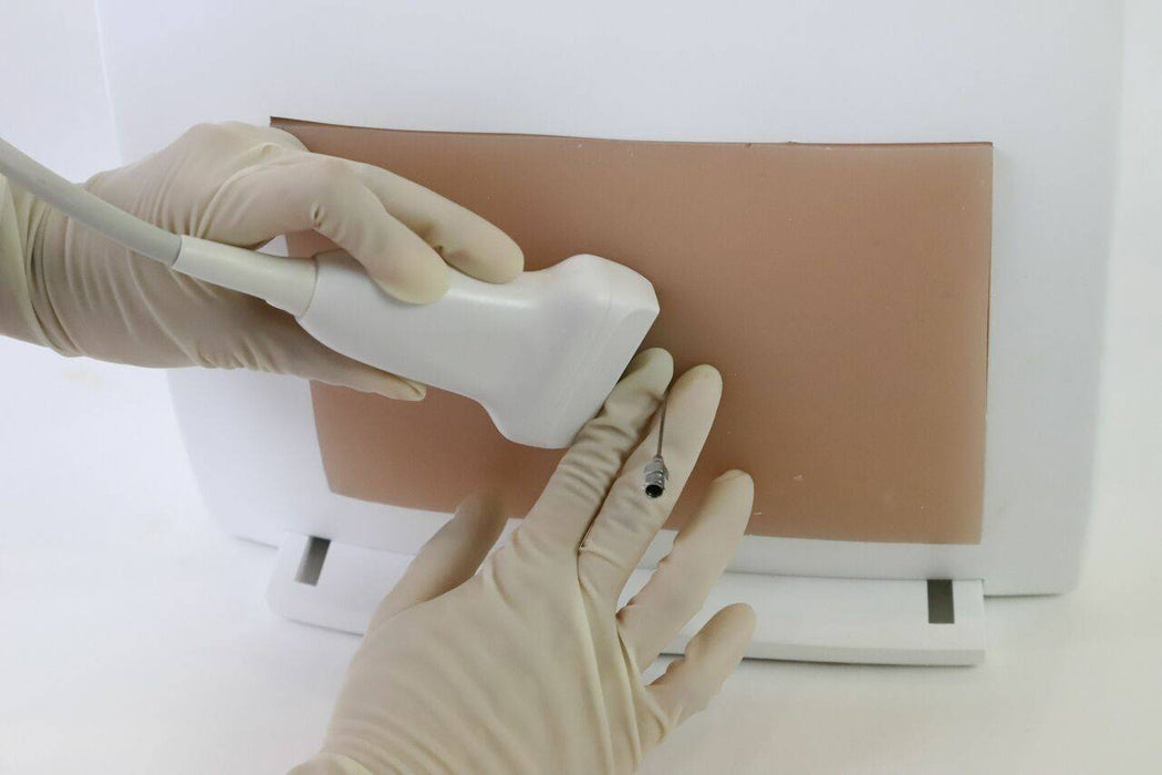 Hands in surgical gloves maneuver an ultrasound probe on skin. The probe is being guided for a medical procedure on a white table.