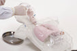 A gloved hand inserts a tube into a transparent anatomical model, revealing pink lungs within. A metal tray sits nearby, set against a stark white background.