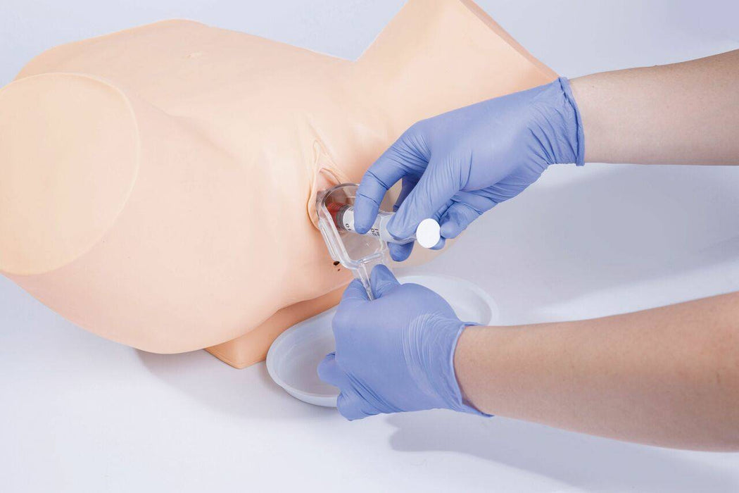 Gloved hands use a syringe on a medical dummy, likely for training, with a dish underneath the object and a plain background.