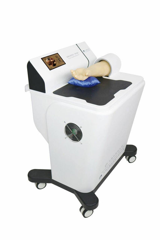 A medical device rests on wheels. A mannequin arm is positioned on a blue cushion atop the machine. The device has a small screen displaying an image.