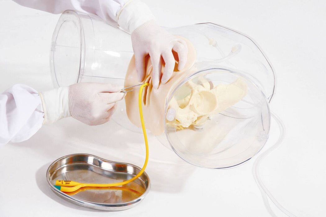 Hands in gloves insert a yellow catheter into a female anatomical model inside of a clear container with a steel tray, which has the text "30ml" written on the side of it, sitting below.