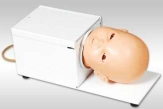 A baby mannequin head rests inside a white box-like device on a white surface; the device appears to be for medical training or practice.