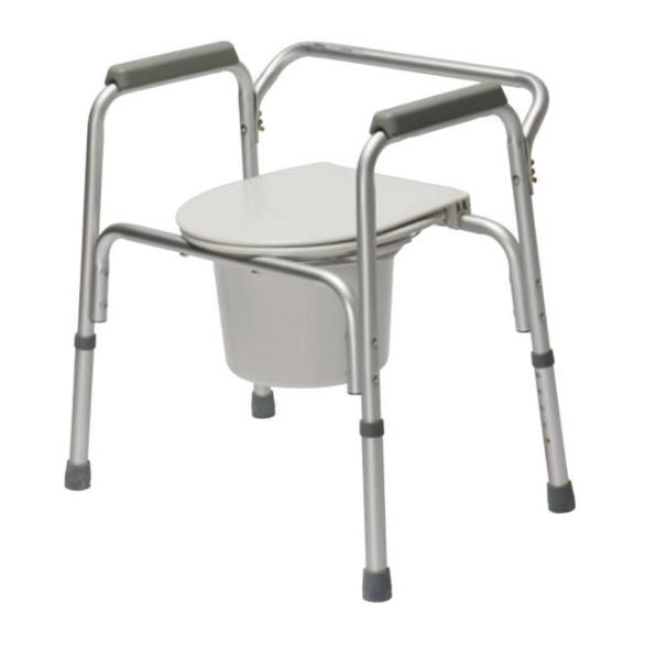 A silver, adjustable commode chair stands, prepared for use, against a plain white background. It has armrests and a container under the toilet seat.