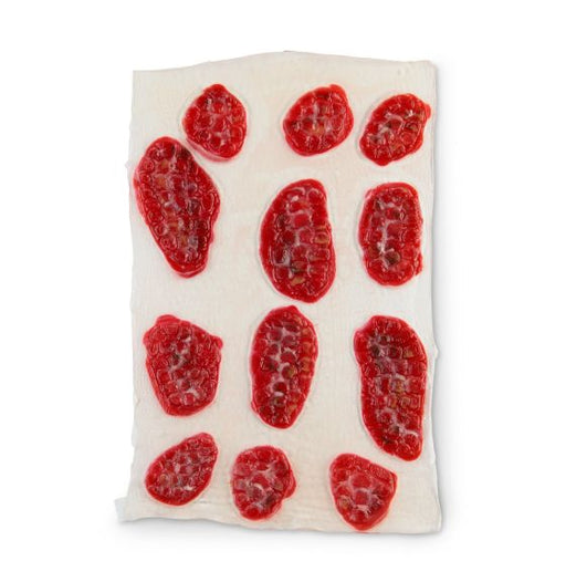 Red objects resembling fruit segments are arranged on a white surface. They appear to be drying or preserving. The context is a light-colored, possibly absorbent, background.