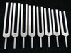 Eleven tuning forks are arranged in a slightly curved row against a black background. They appear to be made of metal and are ready for use.