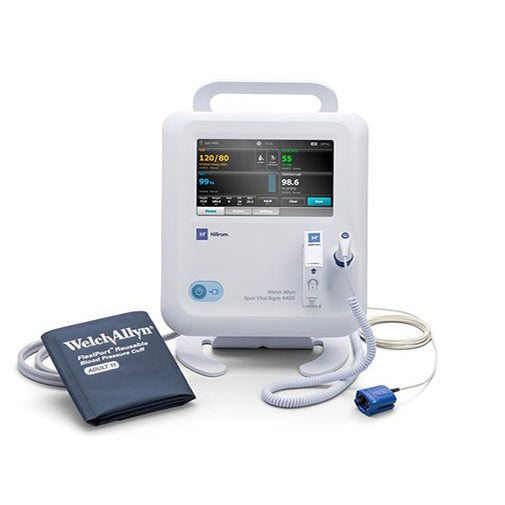 A Welch Allyn vital signs monitor sits on a white surface. The monitor displays patient vitals on a screen, and is connected to a blood pressure cuff labeled "Welch Allyn FlexiPort Reusable Blood Pressure Cuff ADULT 11" and a blue pulse oximeter sensor.