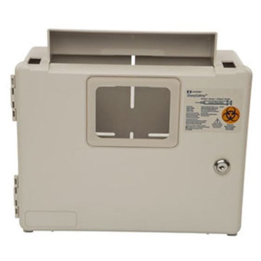 A beige sharps container has slots at the top and a central opening with horizontal and vertical guides; a warning label with a biohazard symbol is affixed to its side.